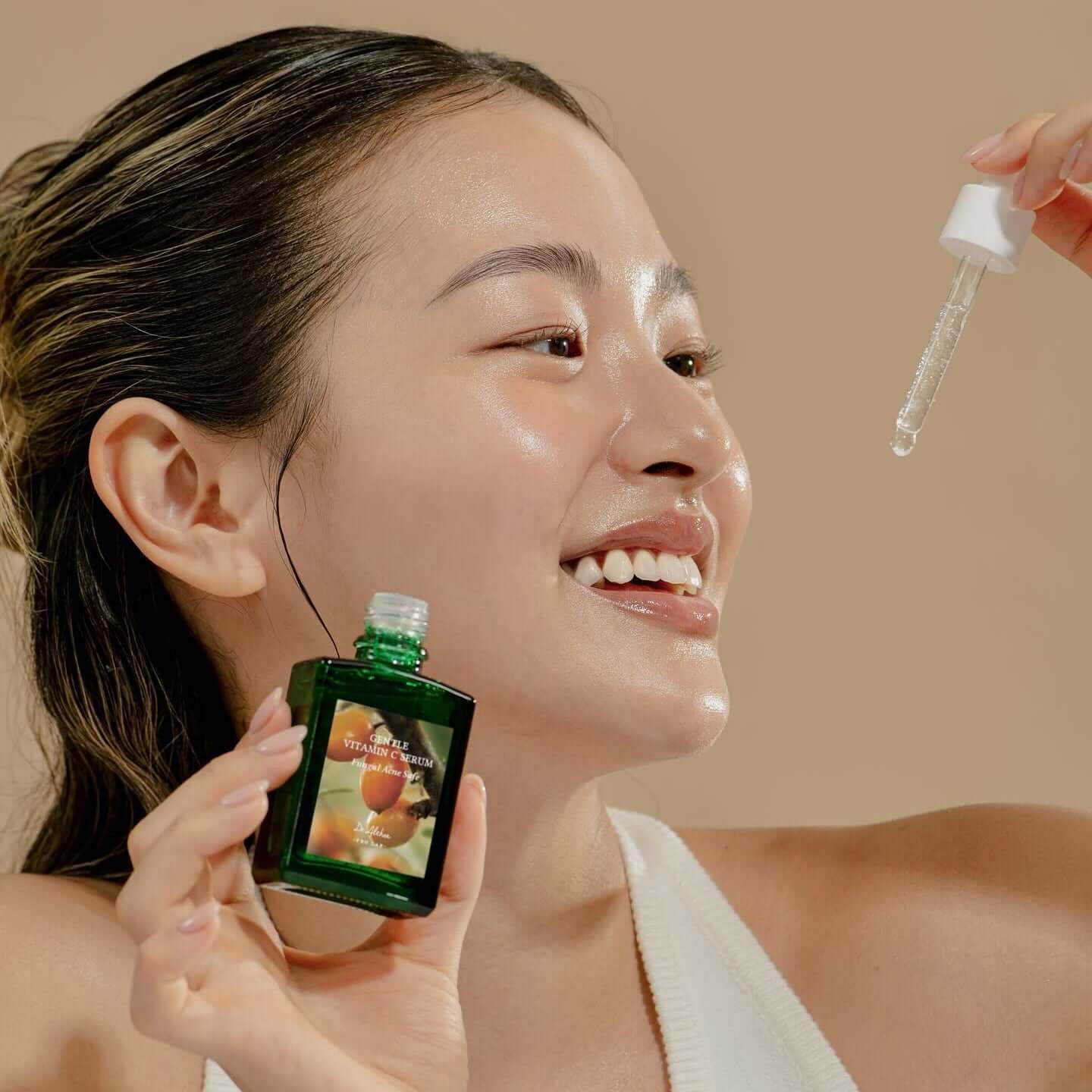 Smiling woman applying DR.ALTHEA Gentle Vitamin Serum 30ml with dropper, showcasing skincare routine.