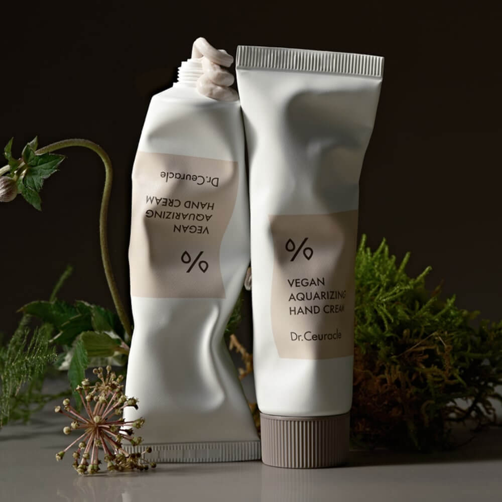 DR.CEURACLE Aqua Rising Hand cream 50ml packaging against a natural background with green plants and flowers.