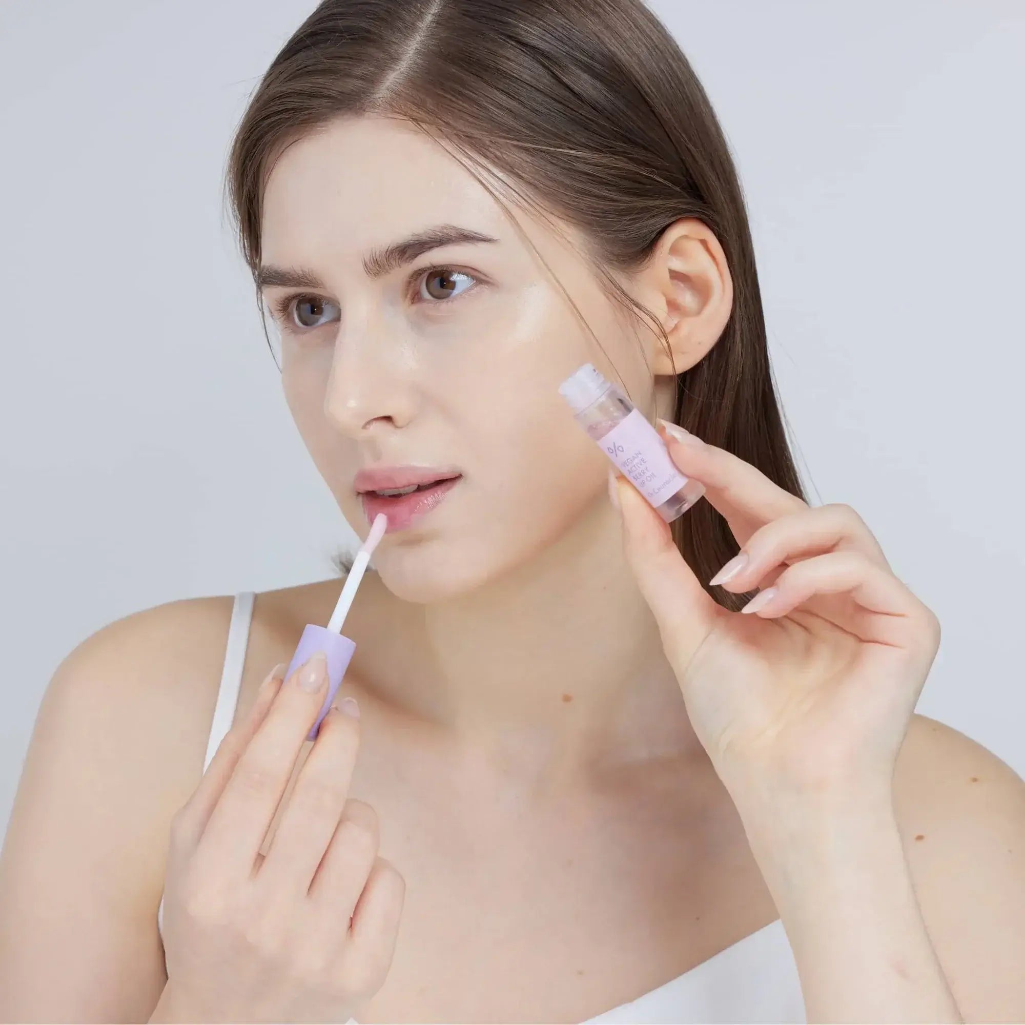 Woman applying DR.CEURACLE Vegan Active Berry Lip Oil for moisturizing lips.