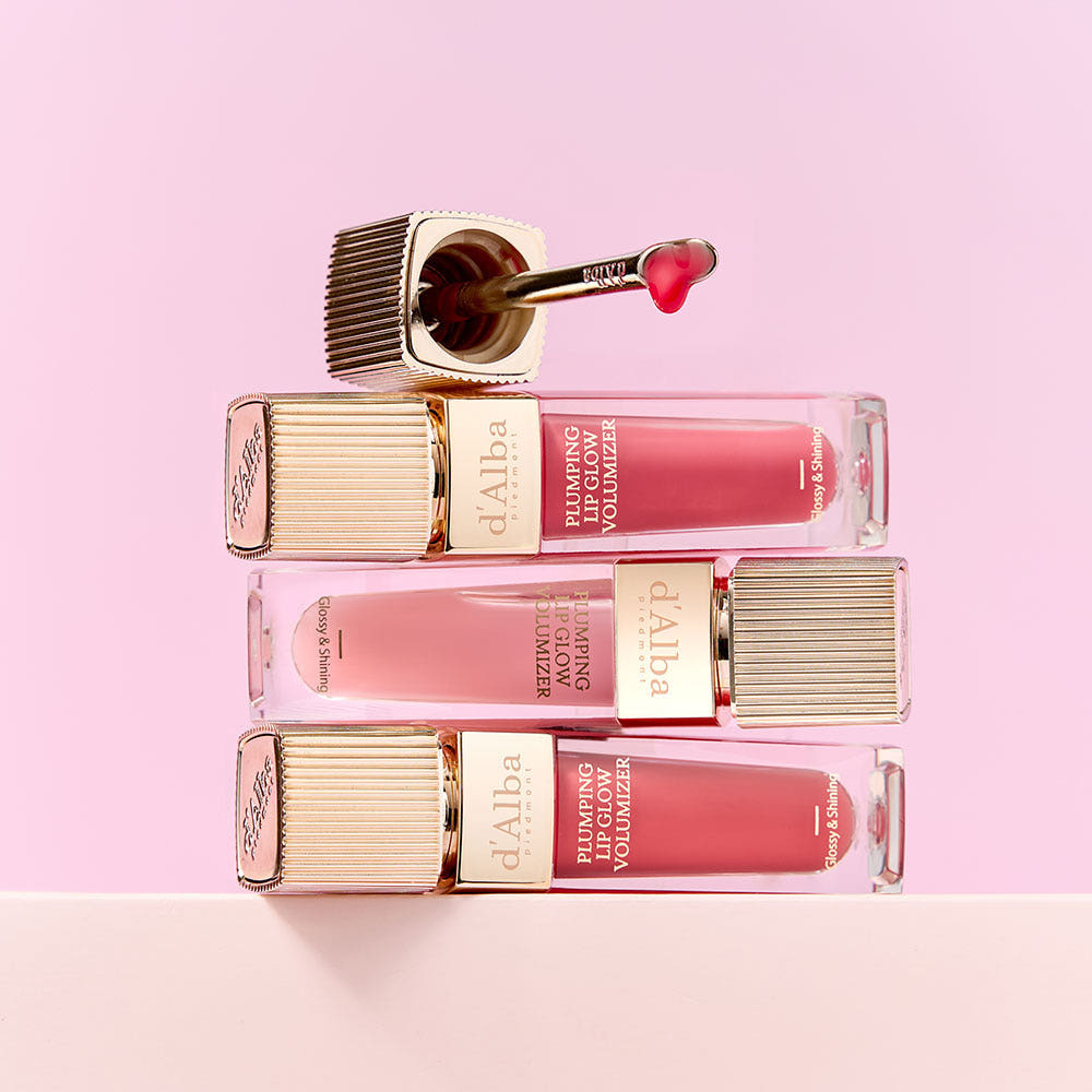 Three bottles of D'ALBA Plumping Lip Glow Mood Volumizer 5ml on a pink background.