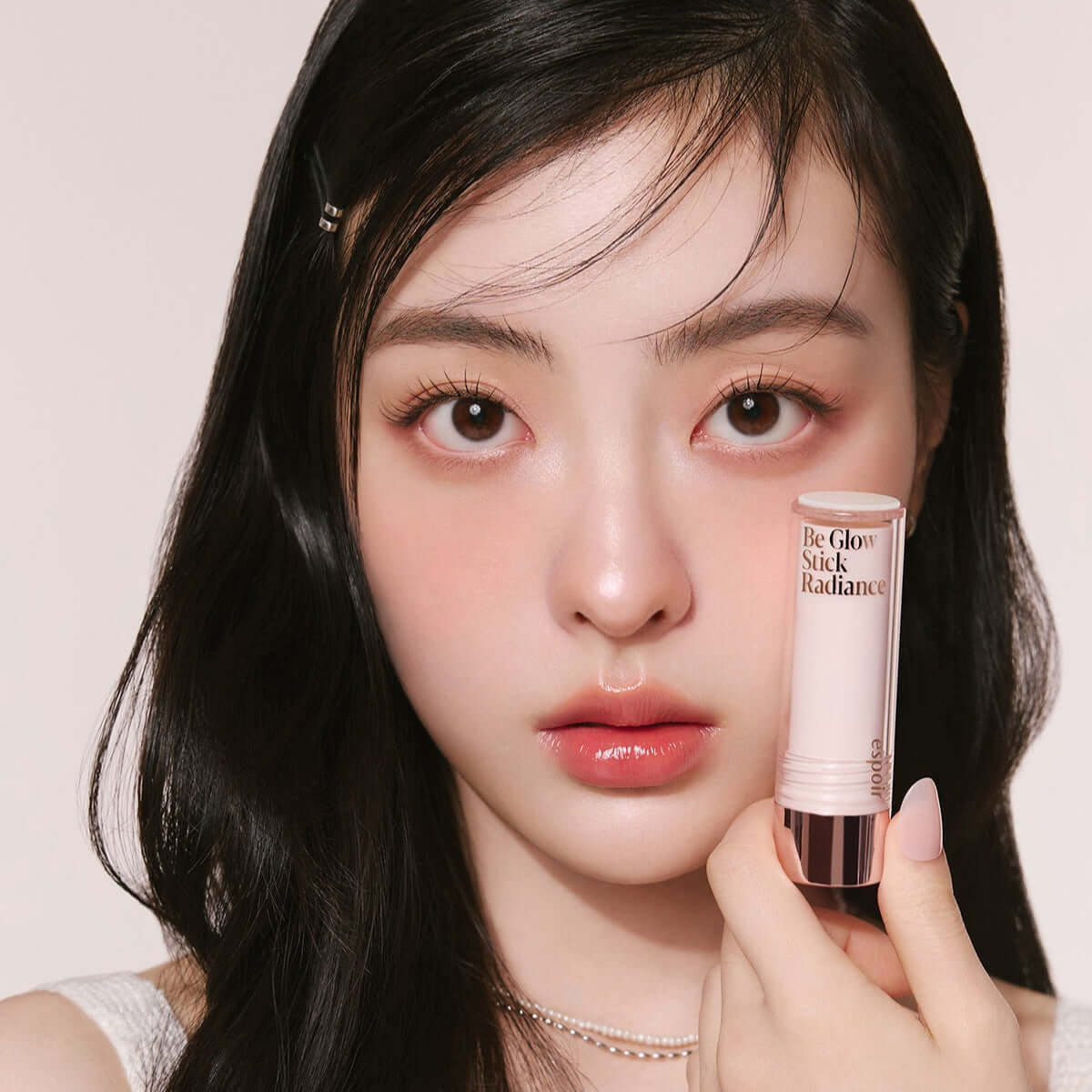 Woman holding ESPOIR BE GLOW STICK RADIANCE near face.