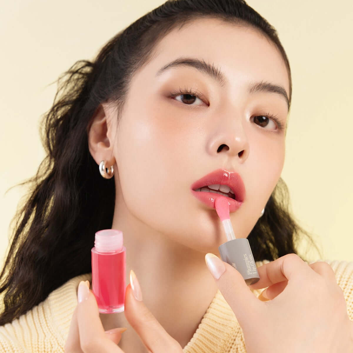 Model applying ESPOIR Plumpies lip gloss with a vibrant pink shade, showcasing glossy finish and moisturizing effect.