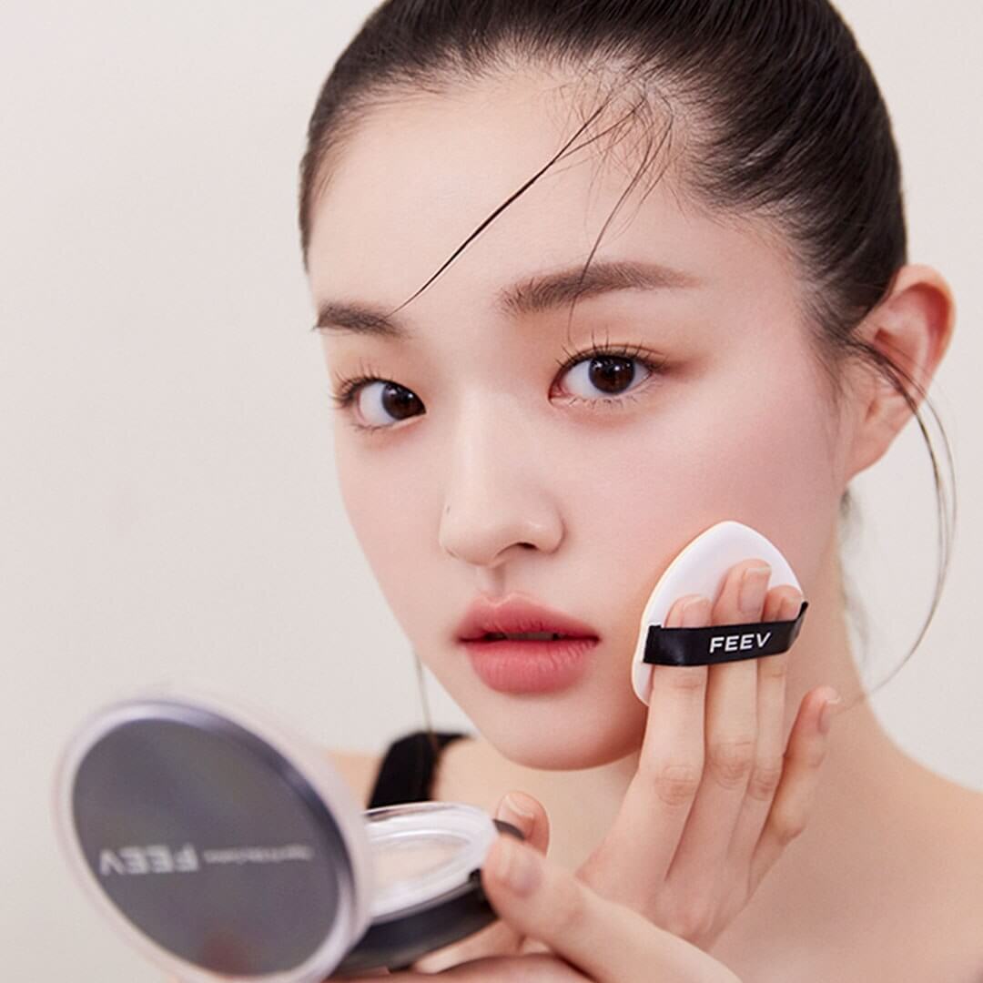 Woman applying FEEV Hyper-Fit Silky Cushion with makeup sponge for flawless coverage.