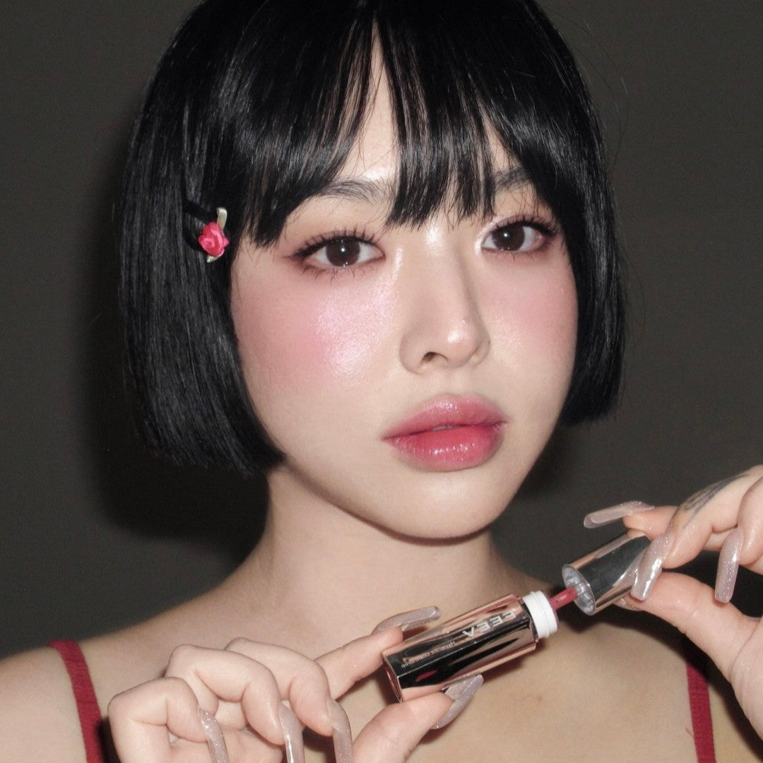 Portrait of a person holding FEEV Hyper-Fit Glam Drop with sleek bob hairstyle and floral clip, showcasing vibrant makeup look.