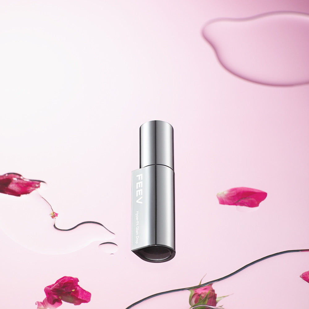 FEEV Hyper-Fit Glam Drop bottle with pink background and rose petals, highlighting luxury skincare product.