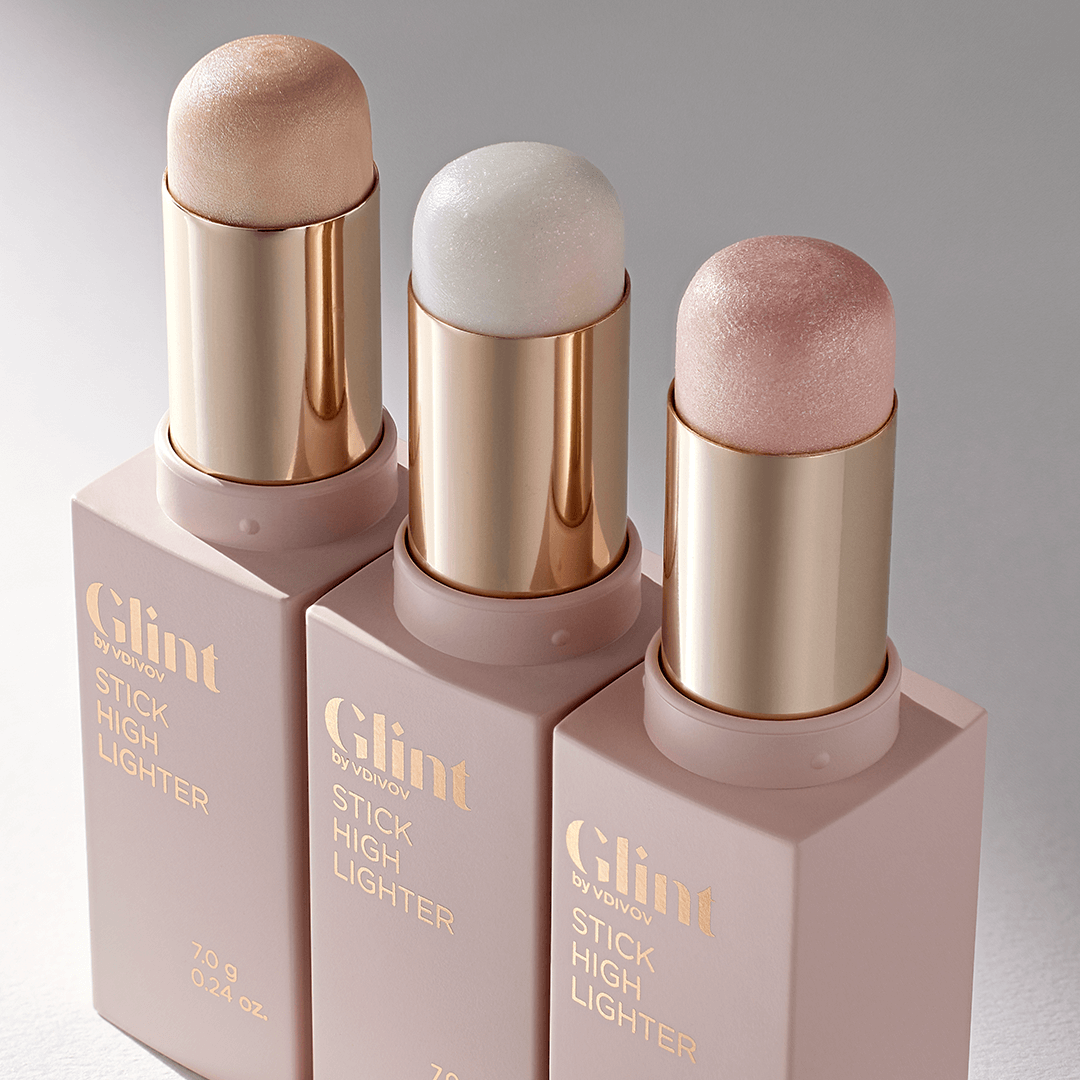 Three shades of GLINT Stick Highlighter in metallic tubes on a glossy surface