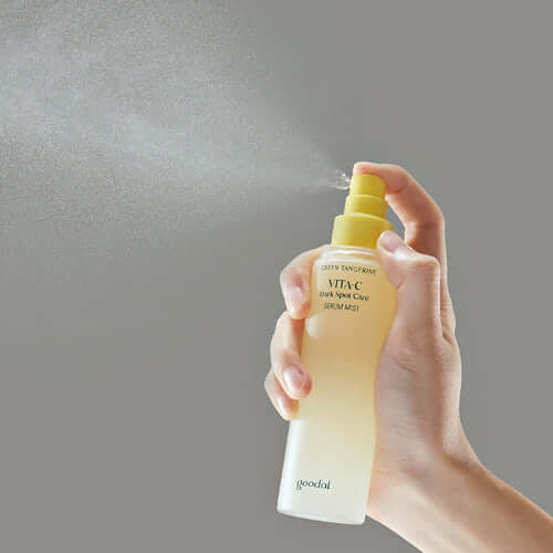 Hand holding and spraying GOODAL Green Tangerine Vita C Serum Mist 100ml against a gray background.