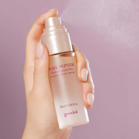 GOODAL Peony Peptide Wrinkle Volume Essence Mist 50ml being sprayed from a bottle held in a hand against a pink background.