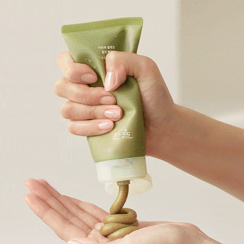 Hands squeezing HANYUL Young Mugwort Cleansing absorption Pack Foam onto palm from a green tube, highlighting product use.