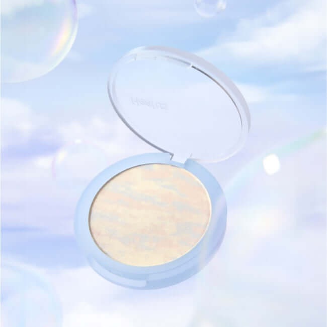 Open compact of HEALUS Breath Cloud Powder against a soft, dreamy sky background with subtle cloud and bubble effects.