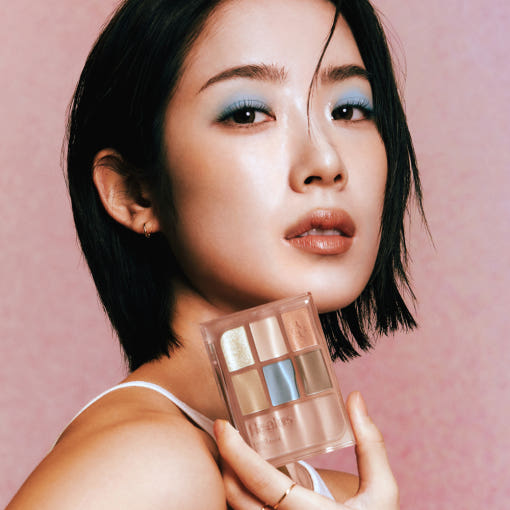 Woman holding HEALUS Color Pairing Palette 10g with assorted eyeshadows against a pink background