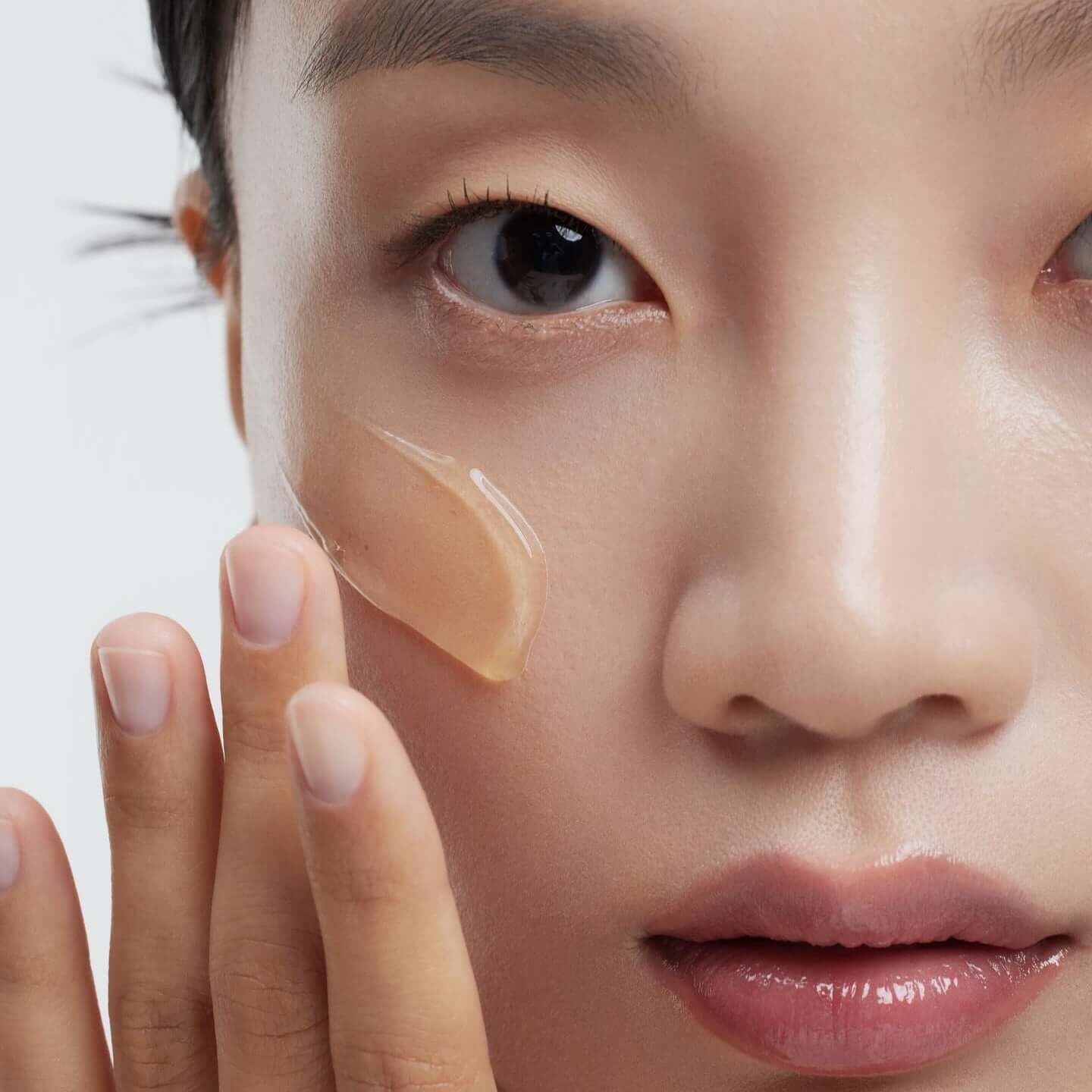 Close-up of a woman applying HUXLEY Biosys 360 Ampoule to her cheek for skincare treatment