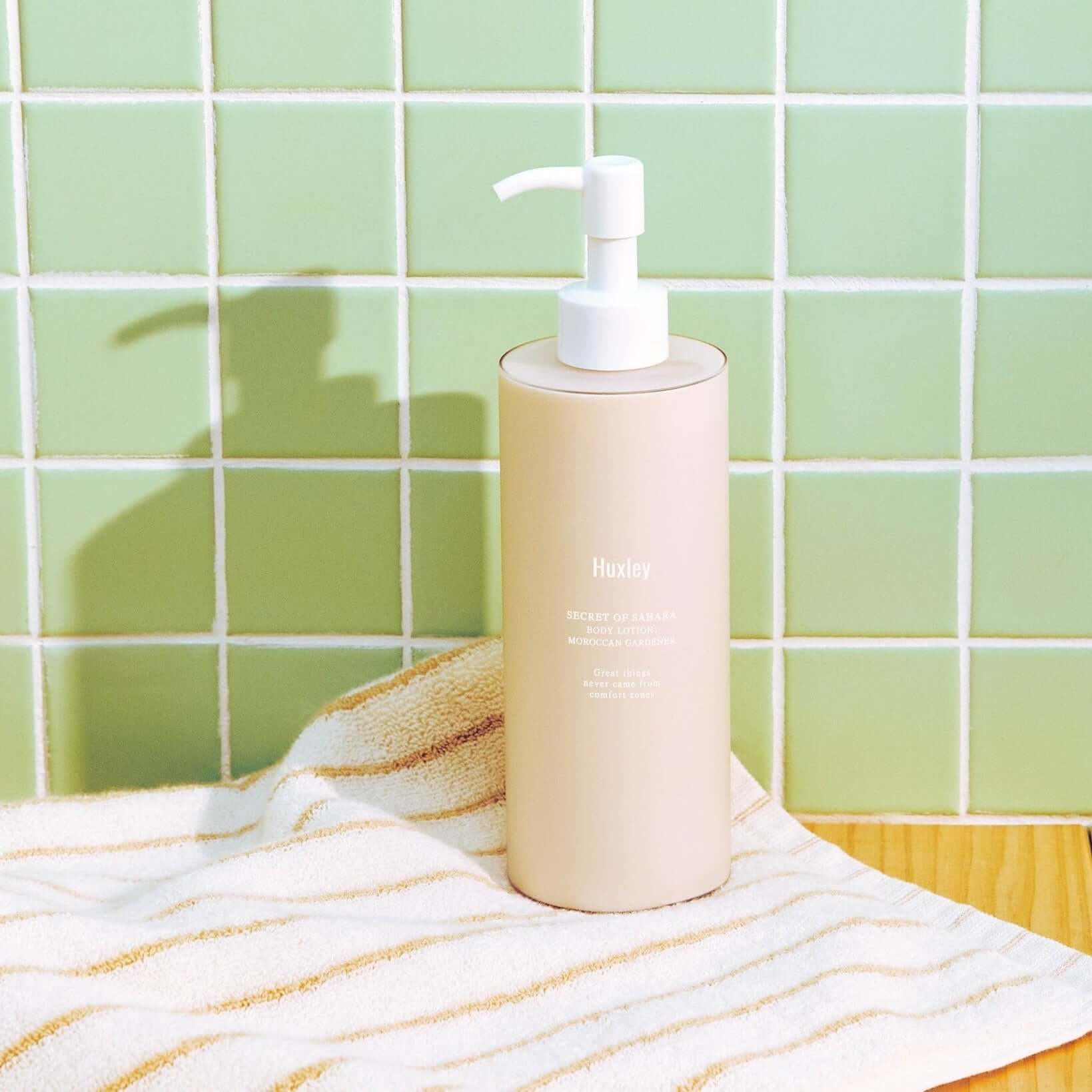 HUXLEY Body Lotion Blue Madina Tangerine bottle on a bathroom counter next to a striped towel.