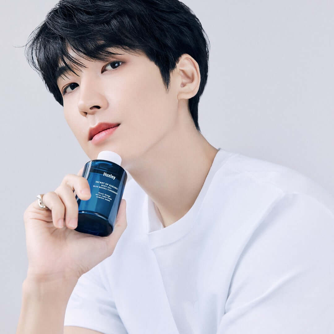 HUXLEY Body Oil Blue Medina Tangrine held by a person in a white shirt, highlighting the product's sleek packaging.