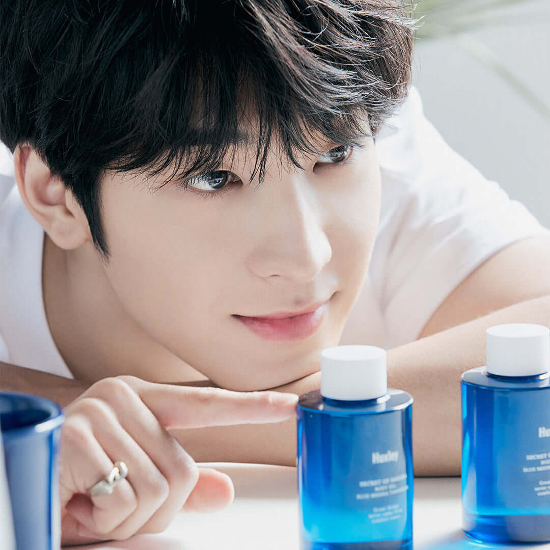 Person admiring HUXLEY Body Oil Blue Medina Tangrine displayed on a table.