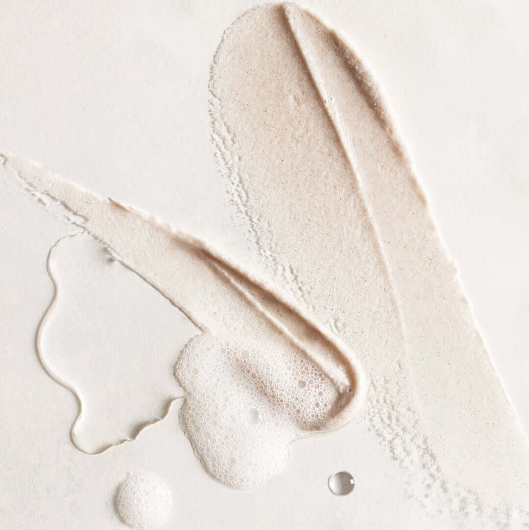 Texture of HUXLEY Body Scrub Moroccan Gardener showing creamy exfoliating formula with bubbles on a light background.