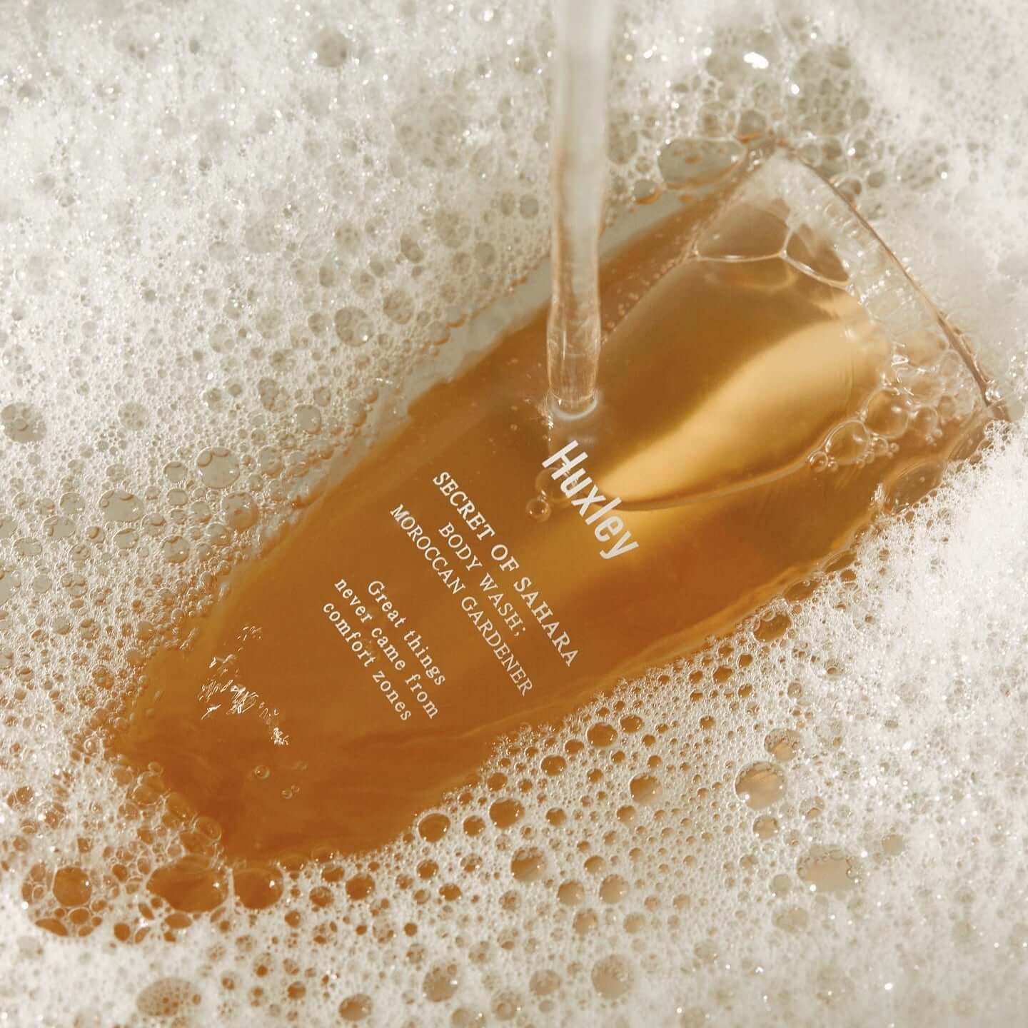 HUXLEY Body Wash Blue Medina Tangerine in foamy bath setting, showcasing luxurious bottle design and branding in use.