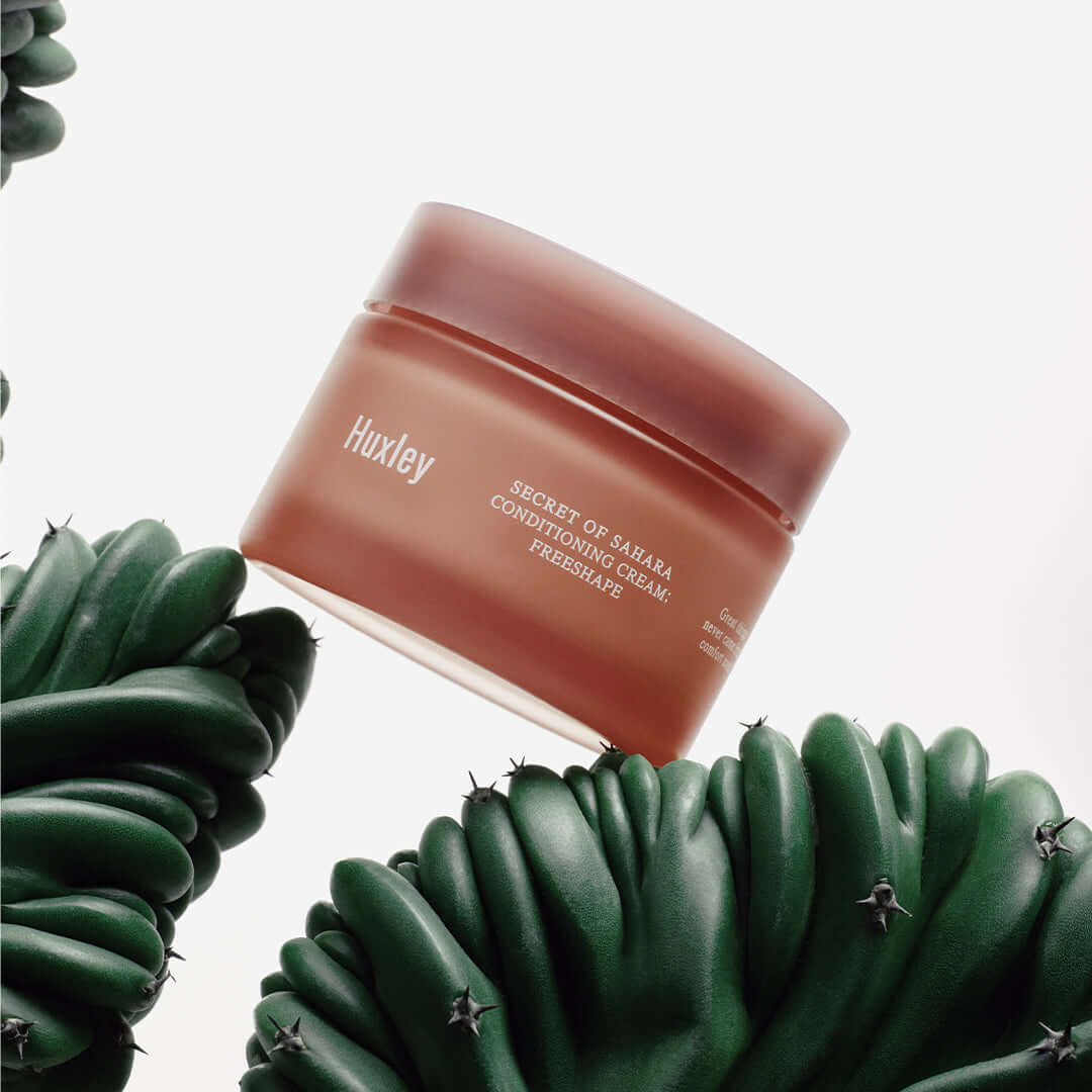 HUXLEY Conditioning Cream Preshape in a brown jar surrounded by green succulents