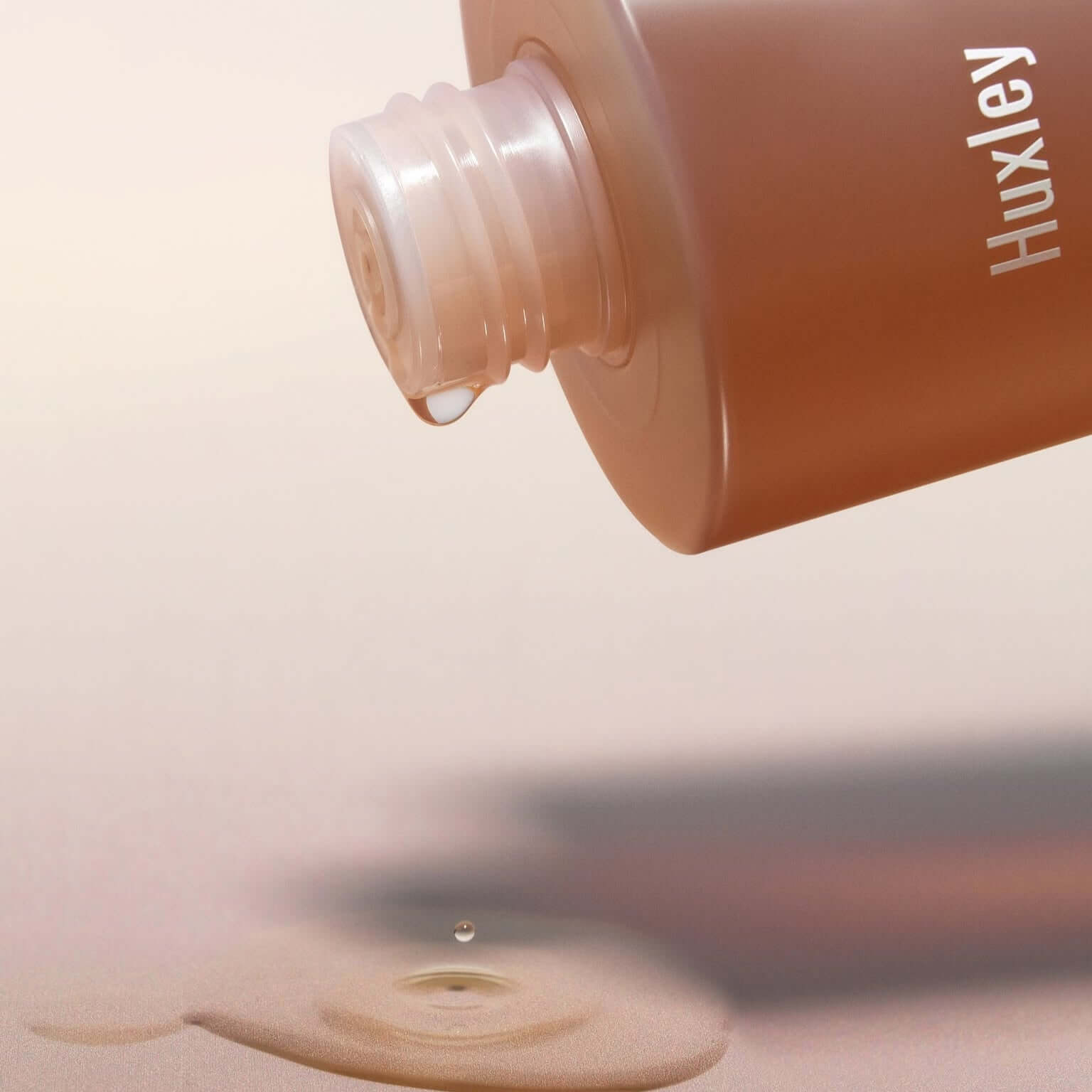 HUXLEY Conditioning Essence Toner Preshape bottle with liquid pouring, highlighting the skincare product's hydrating properties.