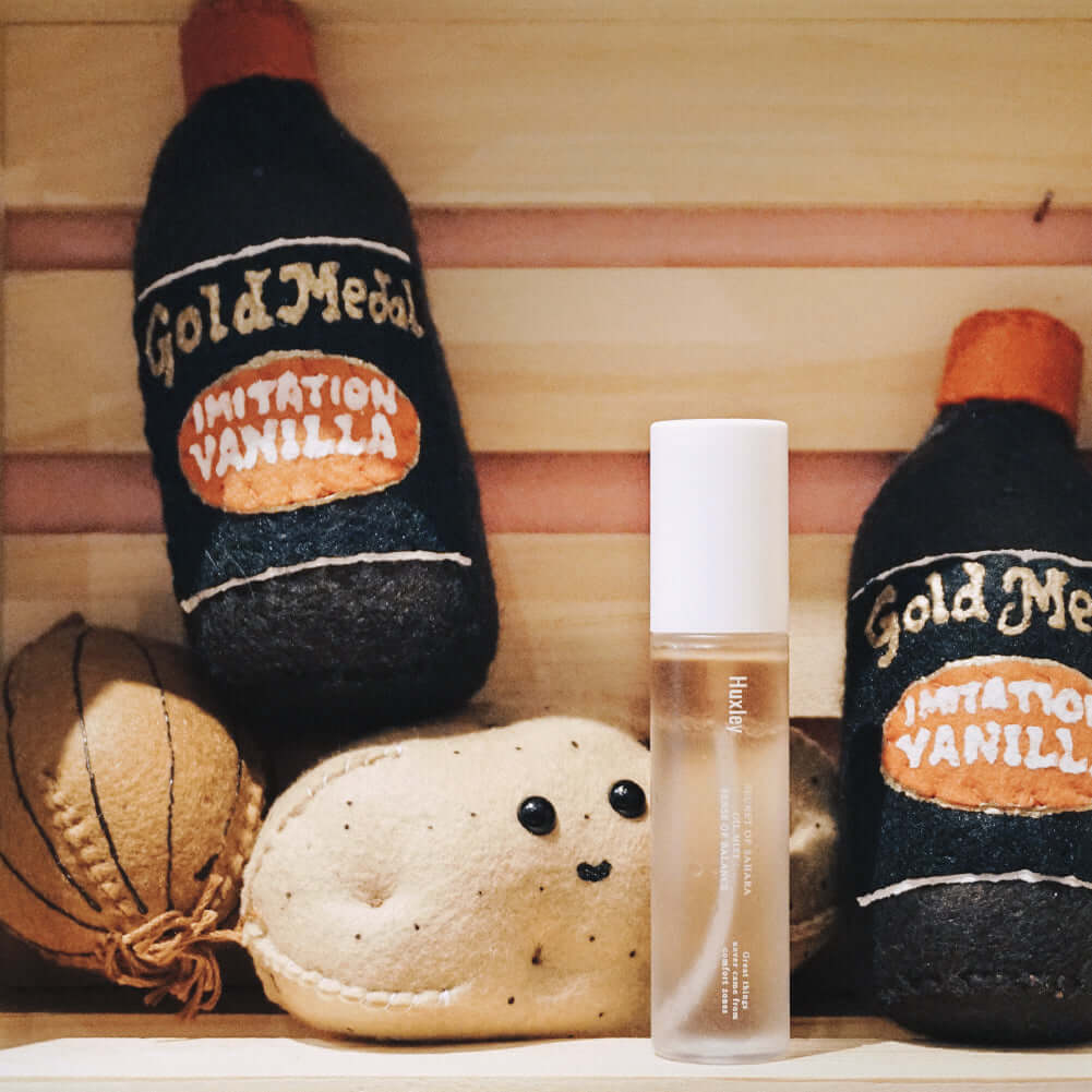 HUXLEY Oil Mist Sense Of Balance displayed with vintage vanilla bottles and plush toy in a wooden shelf scene.