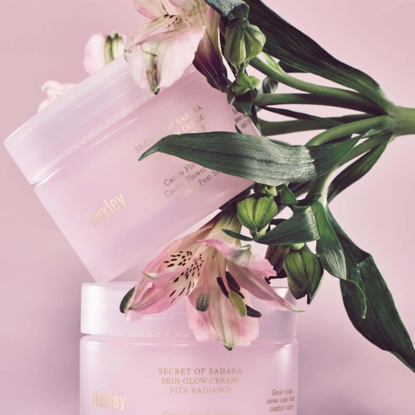 HUXLEY Skin Glow Cream Vita Radiance jars with flowers, promoting enhanced radiance for glowing skin.