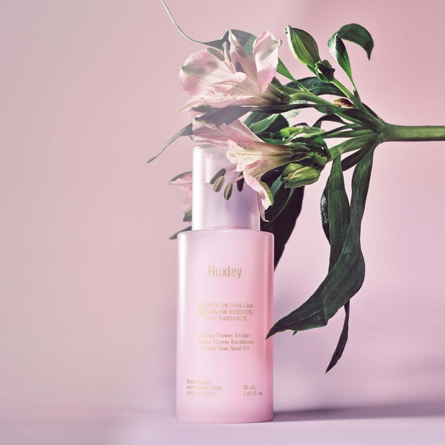 HUXLEY Skin Glow Essence Vita Radiance with floral background, glowing serum bottle promoting radiant skin.