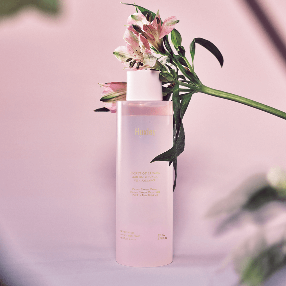 Bottle of HUXLEY Skin Glow Toner Vita Radiance with flowers on a pink background