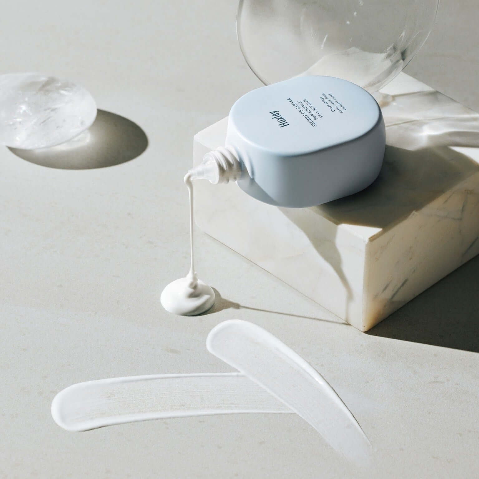 HUXLEY Sun Essence Stay Sun Safe sunscreen pouring on marble surface