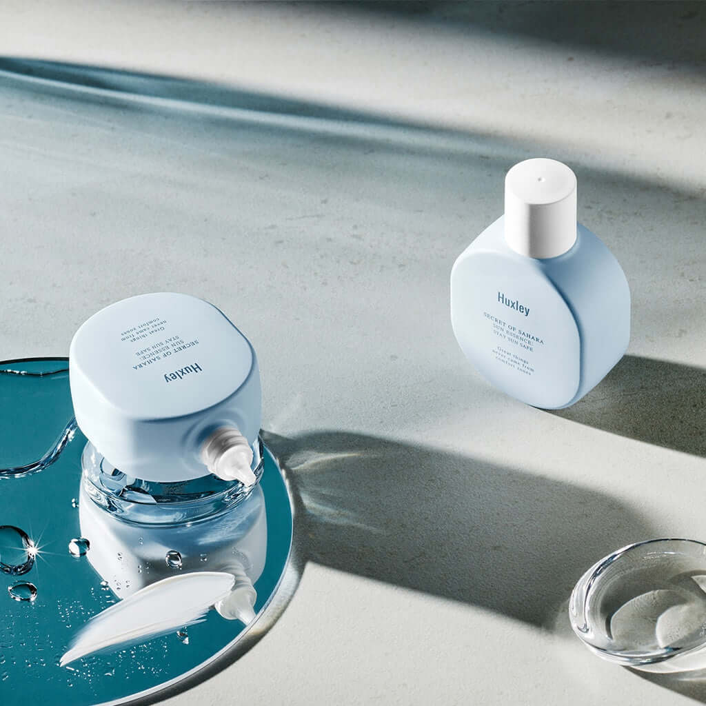 HUXLEY Sun Essence Stay Sun Safe products displayed on a reflective surface with a modern, minimalist design.