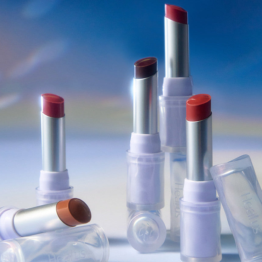 Collection of HEALUS Bare Lip Glow 4g lipsticks in various shades arranged against a soft, blurred background.