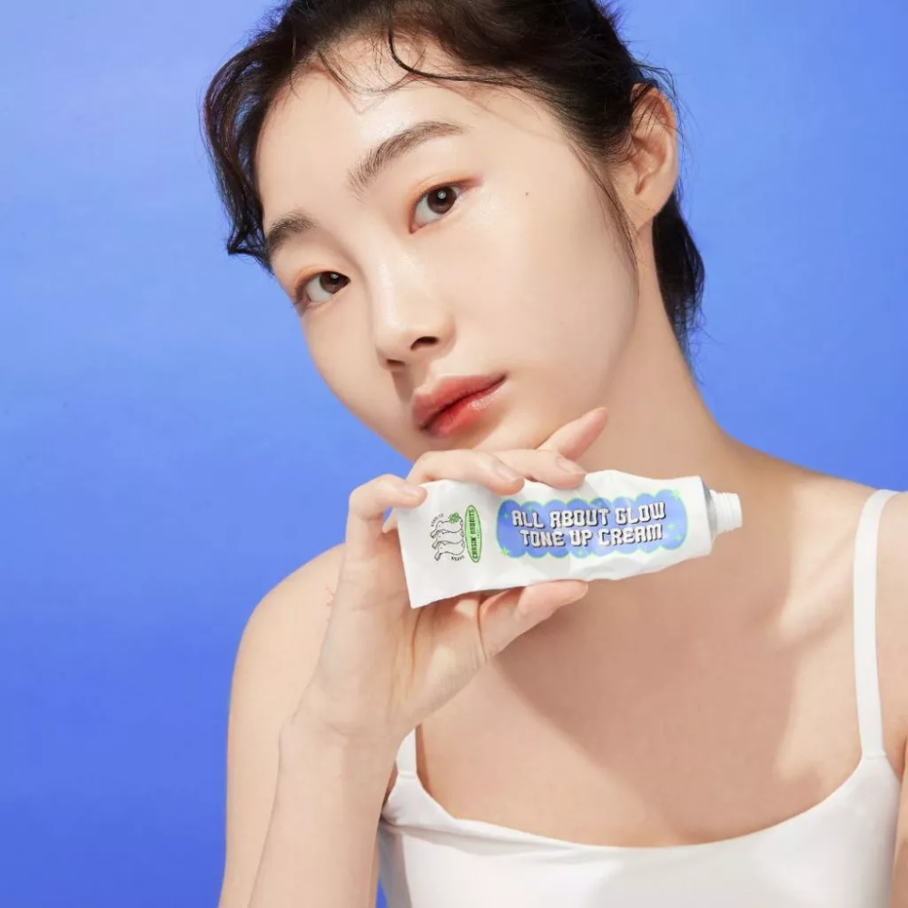 Model holding IT'S SKIN All About Glow Tone Up Cream against a blue background