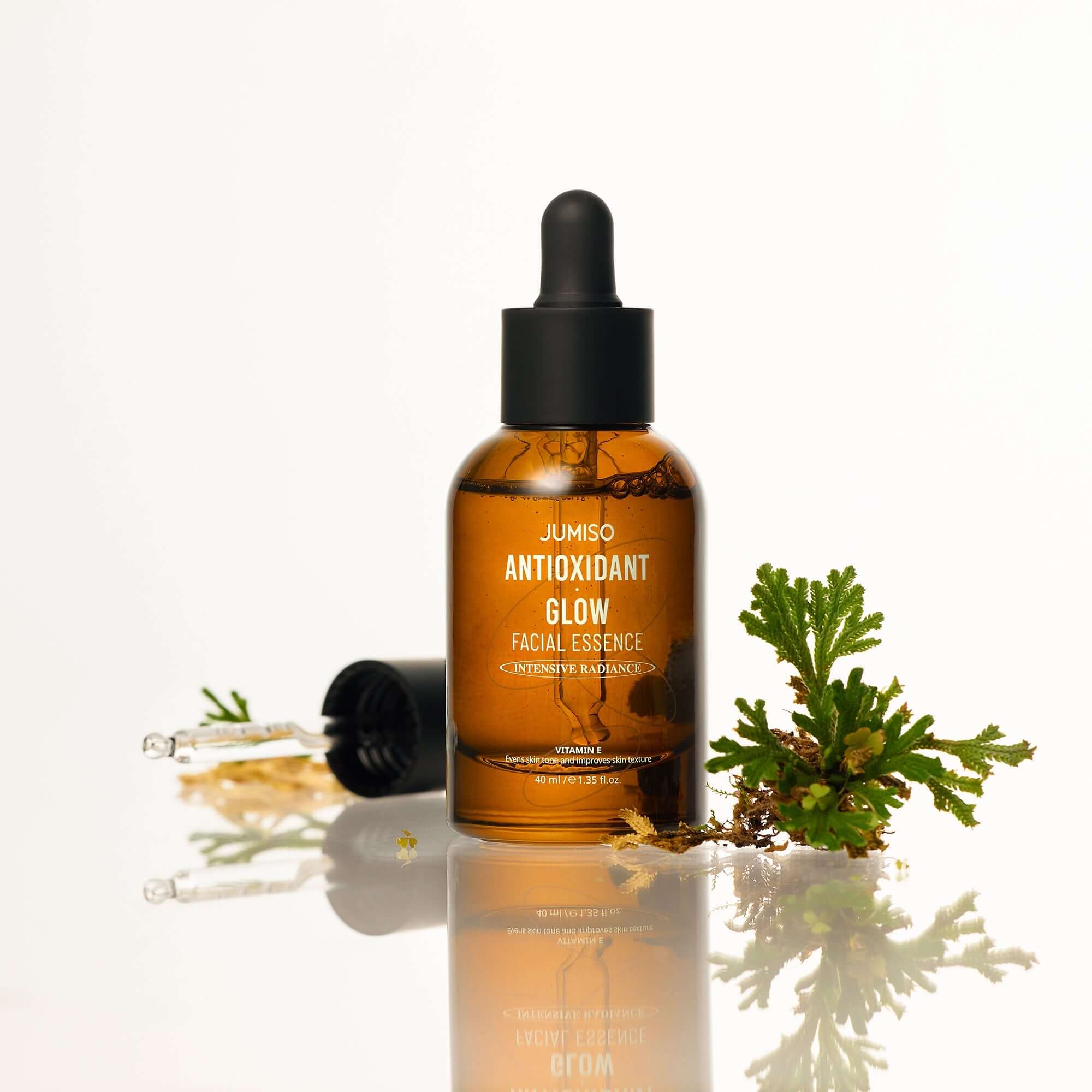 JUMISO Antioxidant Glow Facial Essence bottle with dropper and greenery, enhancing skincare routine.