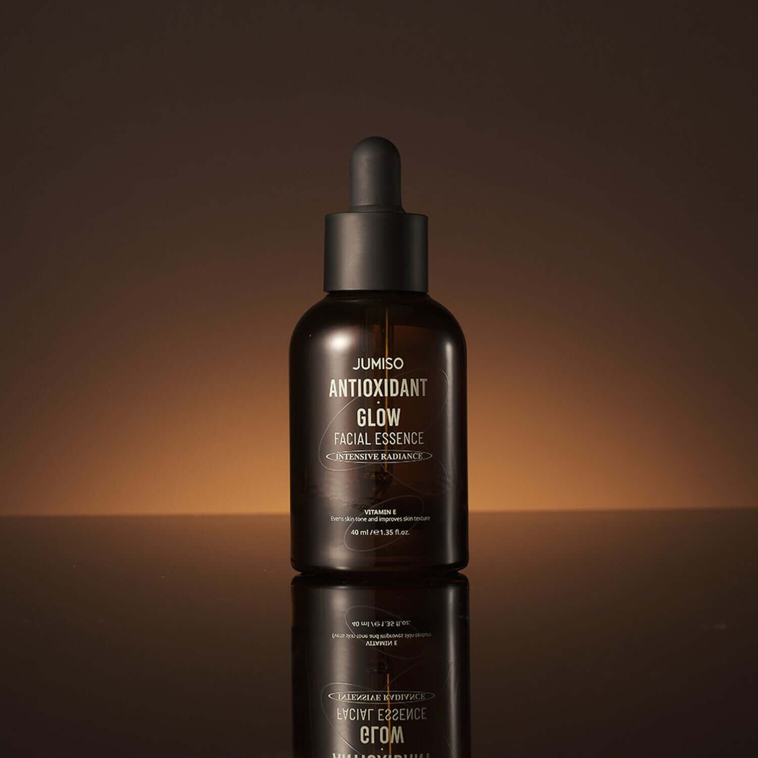 JUMISO Antioxidant Glow Facial Essence bottle on a reflective surface with a warm background