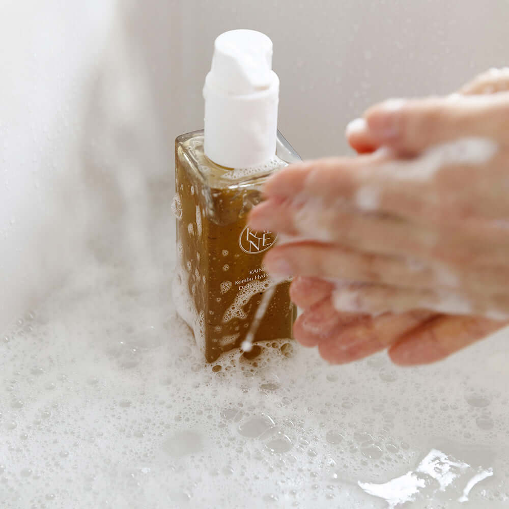 Hands lathering with foam next to KAINE Kombu Hydrating Daily Cleanser 155g bottle