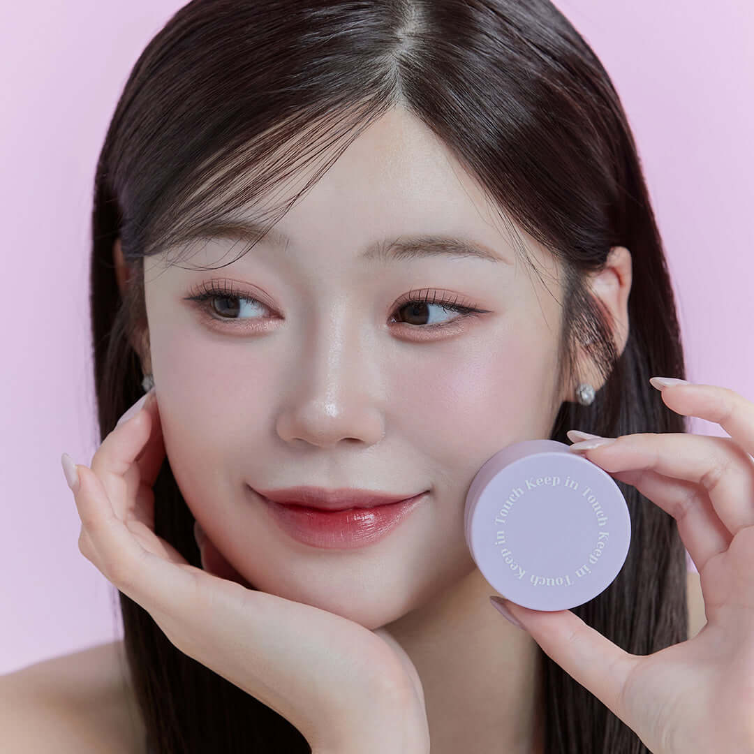 Woman holding KEEP IN TOUCH Mini Pore Eraser Powder with a gentle smile and soft makeup in pastel background.