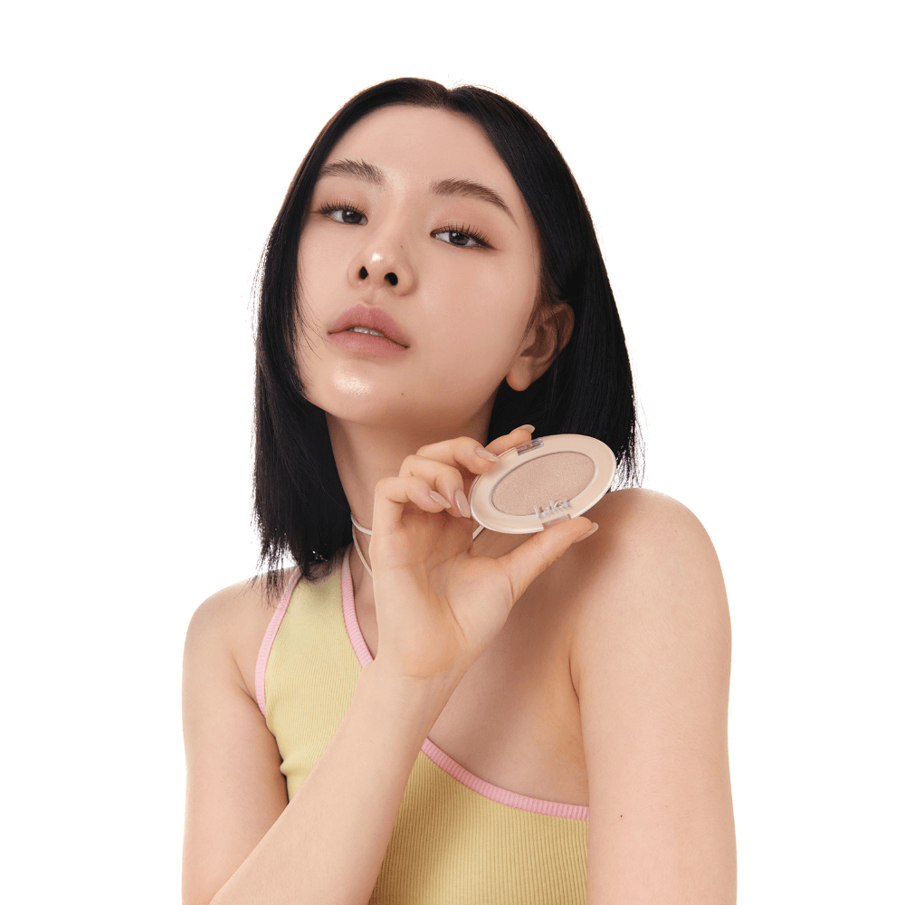 Woman holding LAKA DreamBeam Higlighter in a yellow top, showcasing the product's packaging.