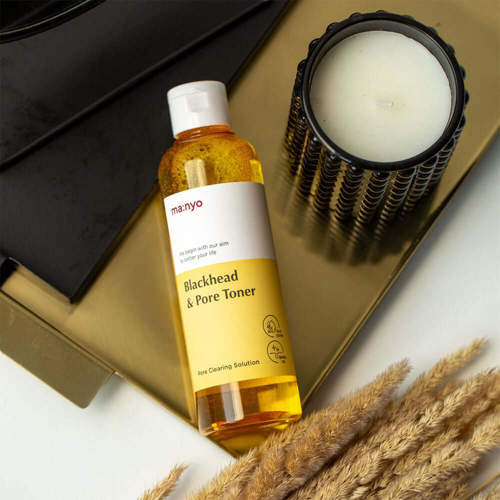 MANYO Blackhead & Pore Toner 210ml bottle on a gold tray next to a candle, featuring skincare benefits for blackheads and pores.