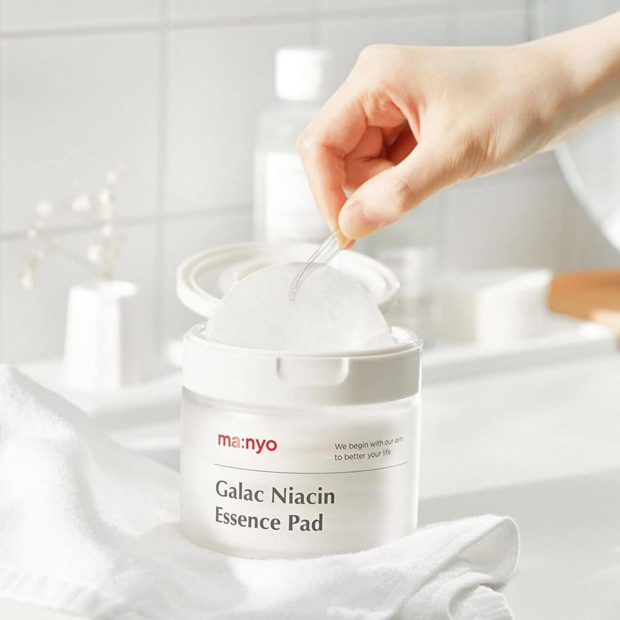 MANYO Galac Niacin Essence Pad 80 Sheets in a bathroom setting, showcasing a hand using the skincare product for facial care.