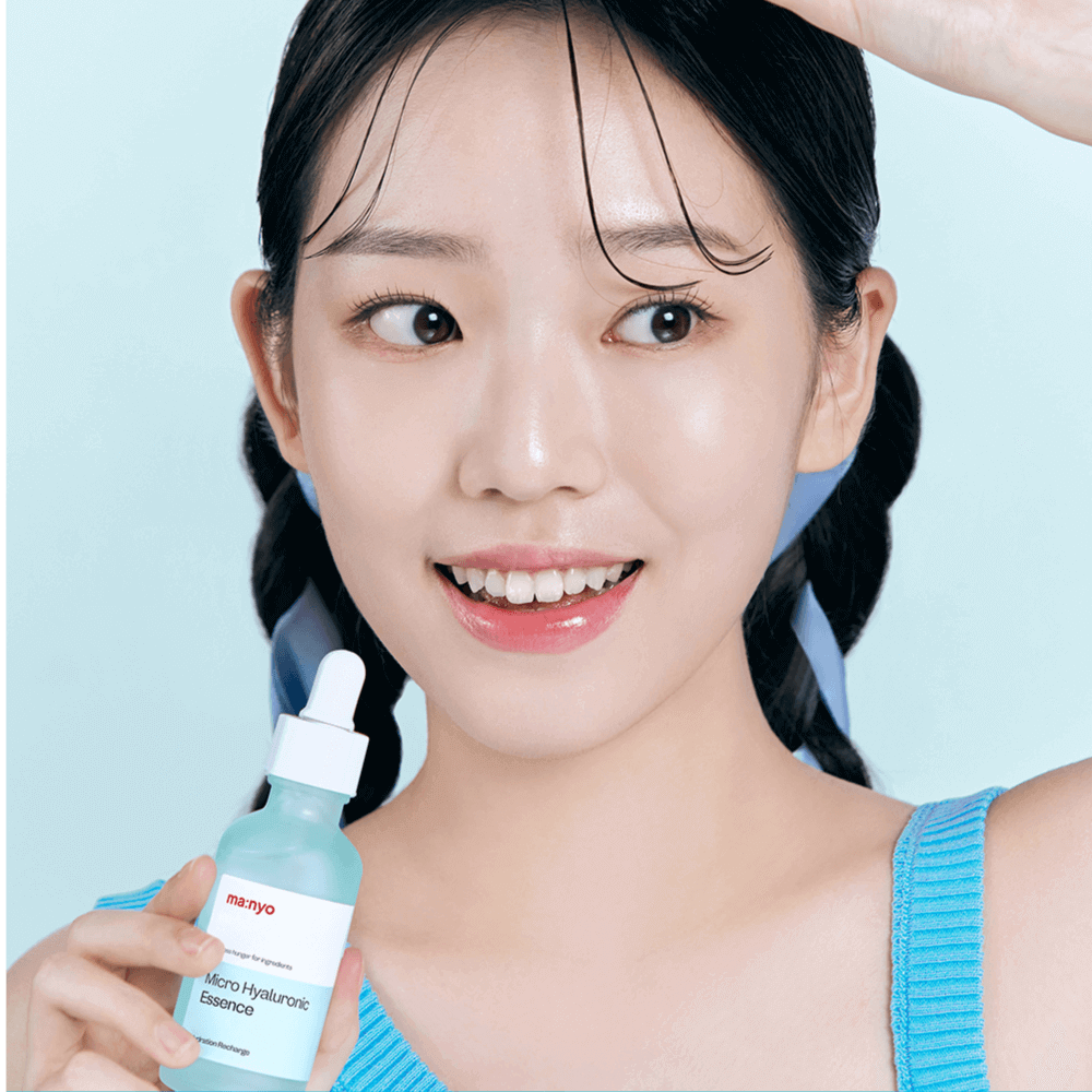 Person holding MANYO Micro Hyaluronic Essence 50ml bottle, smiling, on a blue background.