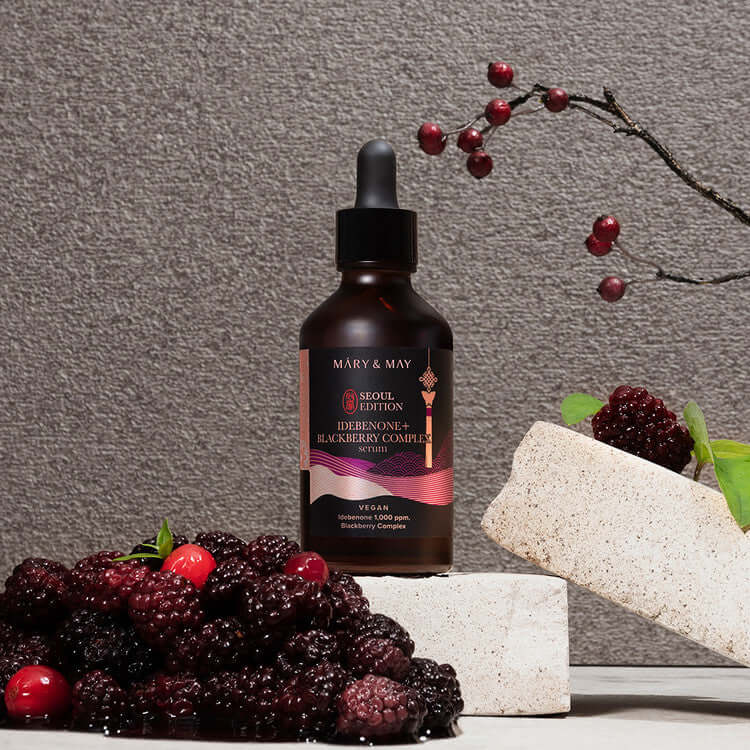 MARY & MAY Idebenone+Blackberry Complex Serum bottle with fresh blackberries on a stone display