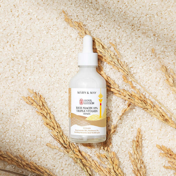 MARY & MAY Rice Niacin 10% triple Vitamin Serum bottle on rice background with wheat accents.