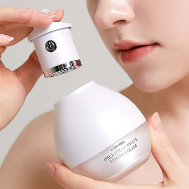 Close-up of person holding MEDITHERAPY Melageran White Toning Cream 50ml + EMS Device next to face, showcasing product use and design.