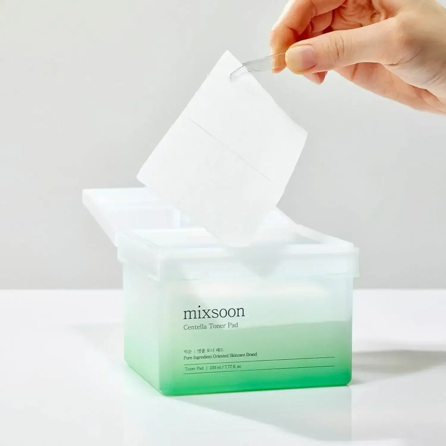 Hand holding MIXSOON Bottle Grass Toner Pad above open box.