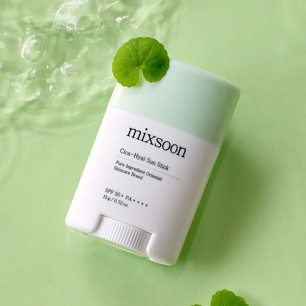 MIXSOON Cica Hyal Sun Stick with green cap, SPF 50+, on a light green background, surrounded by water droplets and a leaf.