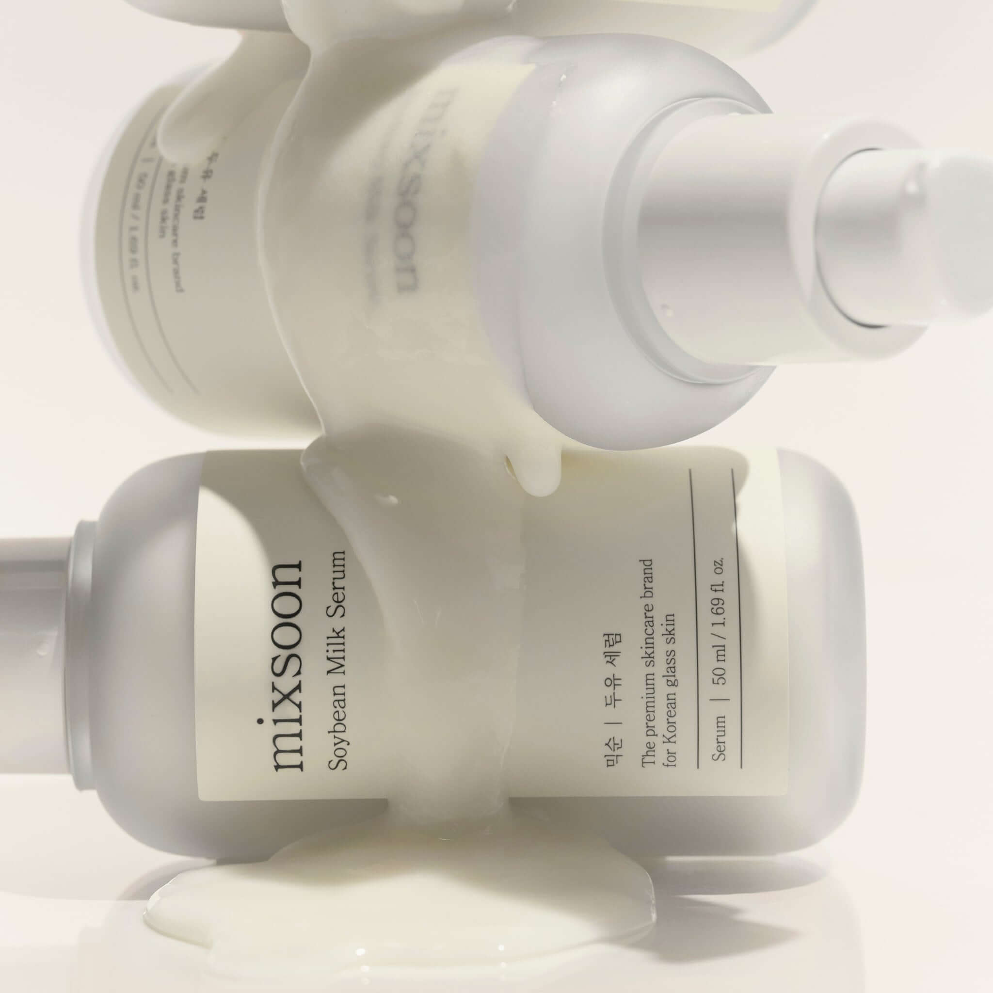 MIXSOON Soybean Milk Serum 50ml bottles with white liquid flowing over them, showcasing skincare product design and packaging.