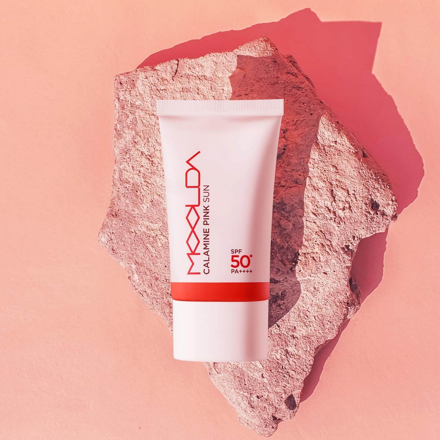 MOOLDA Calamine Pink Sun SPF50+ PA++++ sunscreen tube on a textured pink rock surface.