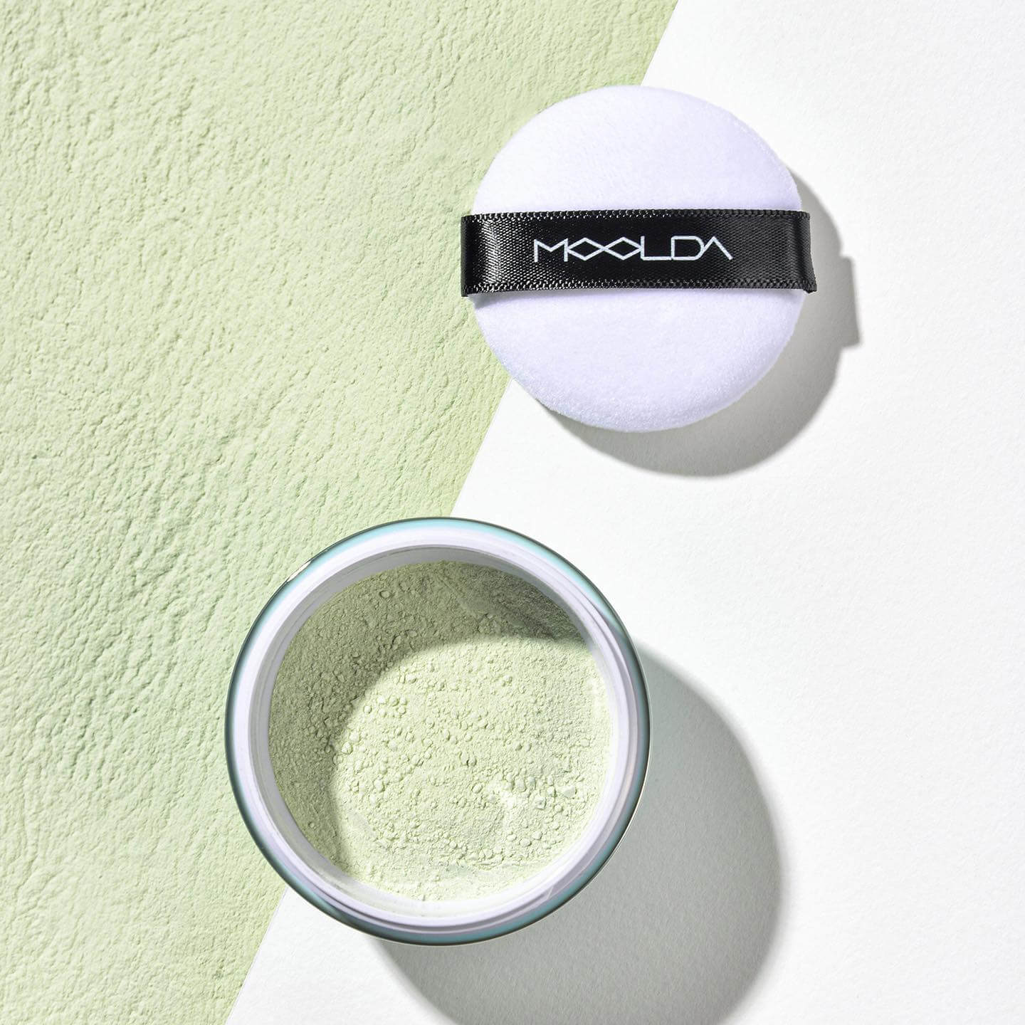 MOOLDA Finishing Powder displayed with applicator on a two-tone background