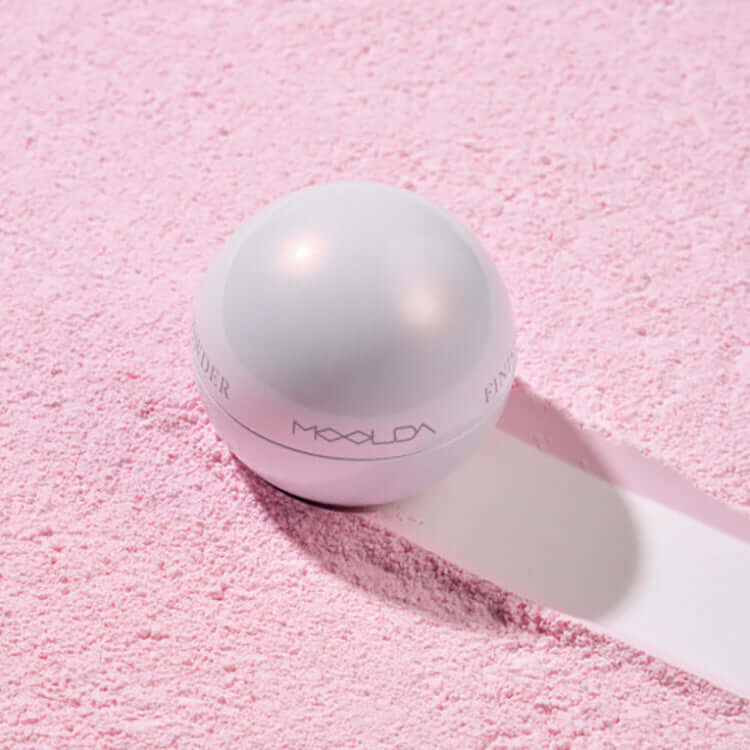 MOOLDA Water Finish Powder on a pink textured surface, highlighting its smooth and stylish packaging.