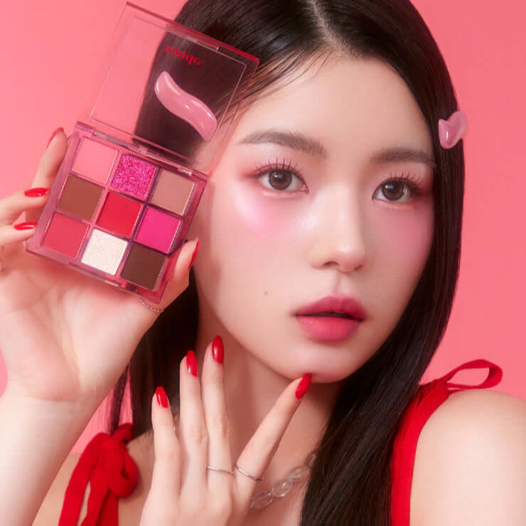 Woman holding MUDE Feel Lively Eyeshadow Palette with pink and red makeup tones.