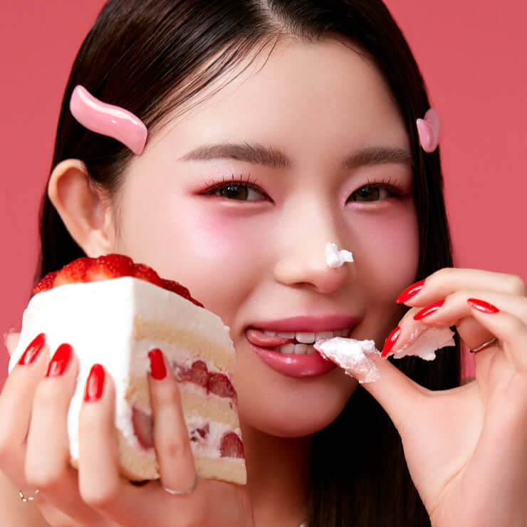 Person enjoying a slice of strawberry cake against a pink background with decorative hair clips.